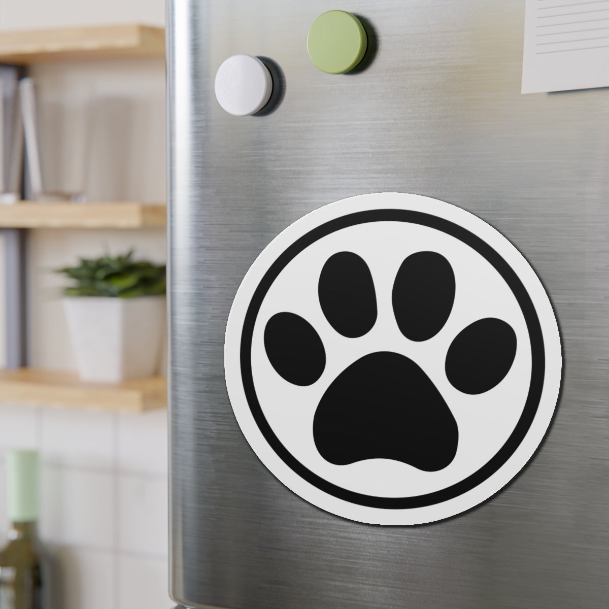 Black-and-white cat paw print die-cut magnet with a circular border, shown on a refrigerator door – Kate Spain design