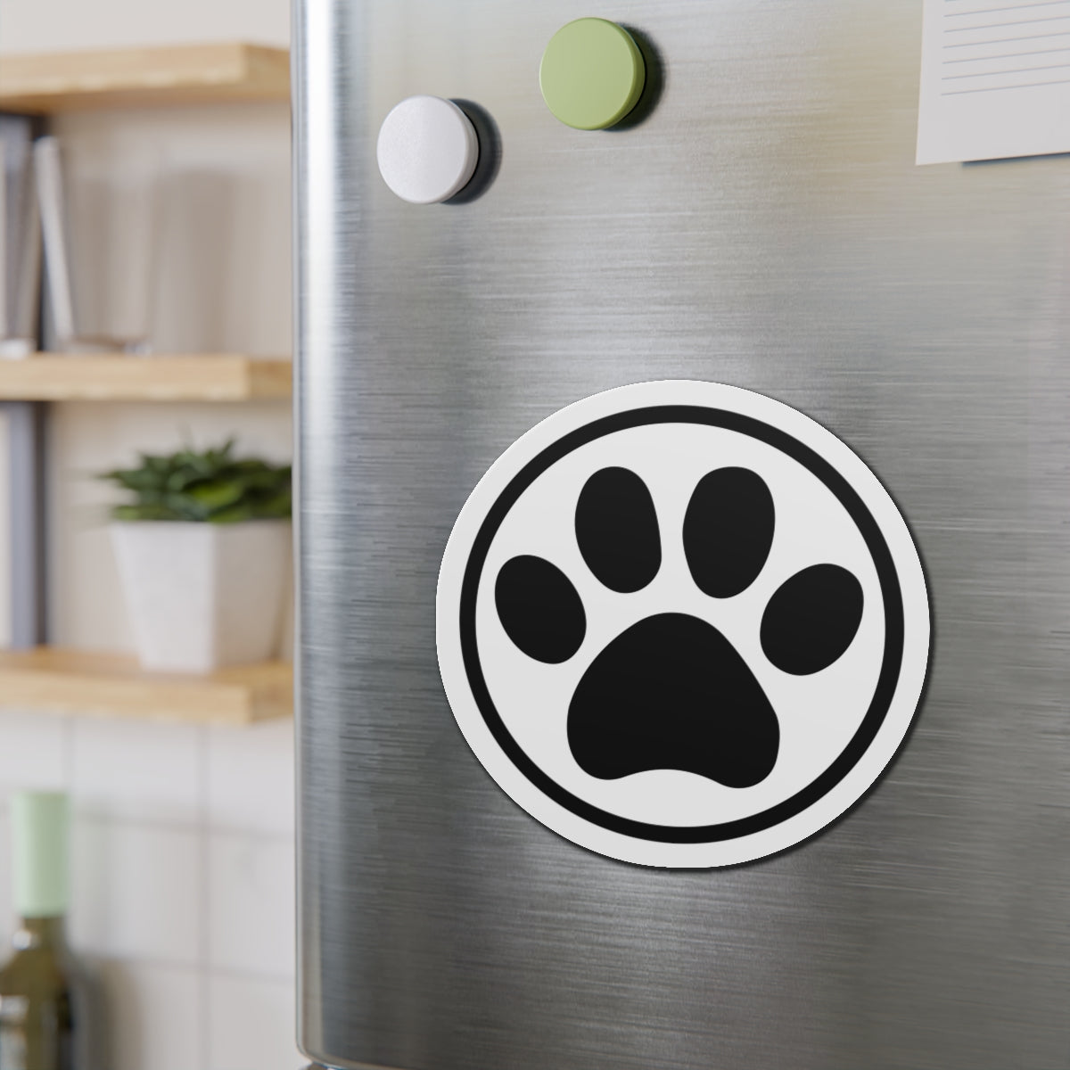Black-and-white cat paw print die-cut magnet with a circular border, shown on a refrigerator door – Kate Spain design