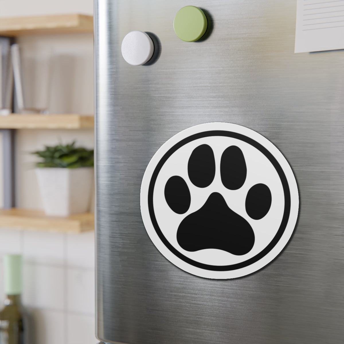 Black-and-white dog paw print die-cut magnet with a circular border, shown on a refrigerator door – Kate Spain design