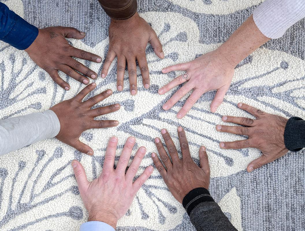 Hands of Kate Spain, Pete Spain, and members of the eye heart hand® rug-making team in India resting together on an eye heart hand® leaf rug