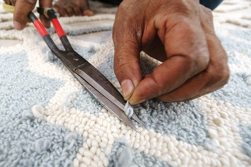 Artisan's hand trimming the wool pile of an eye heart hand® rug with shears