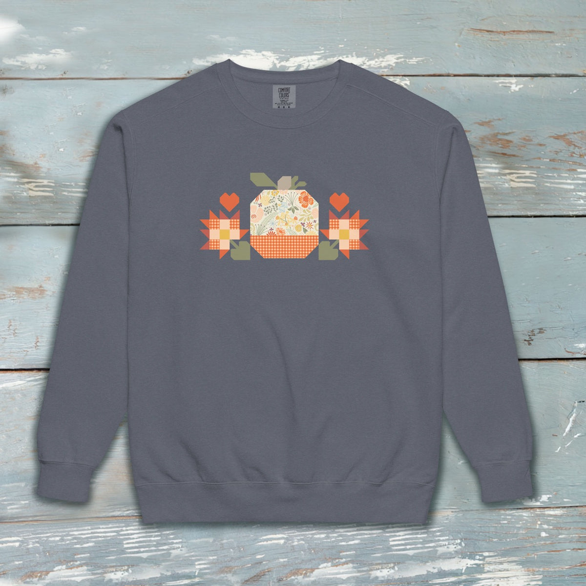 Falling for Fall patchwork pumpkin with quilt-block stars and hearts on a garment-dyed crewneck sweatshirt, styled on weathered wood – Kate Spain design for Pat Sloan