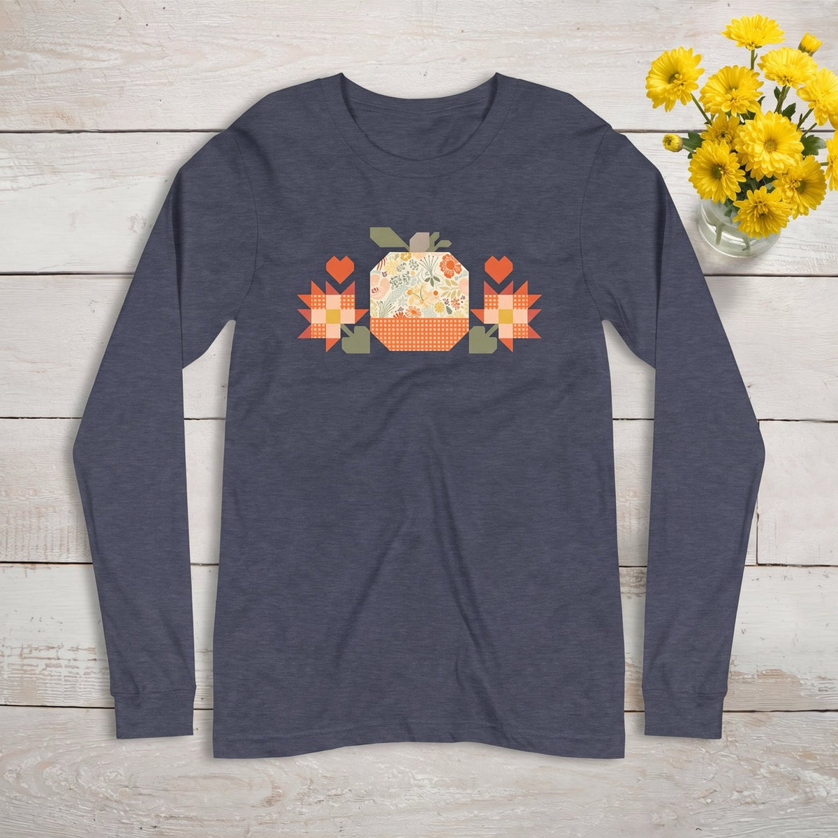 Falling for Fall patchwork pumpkin with quilt-block stars and hearts on a long sleeve t-shirt, styled on wood with yellow flowers – Kate Spain design for Pat Sloan