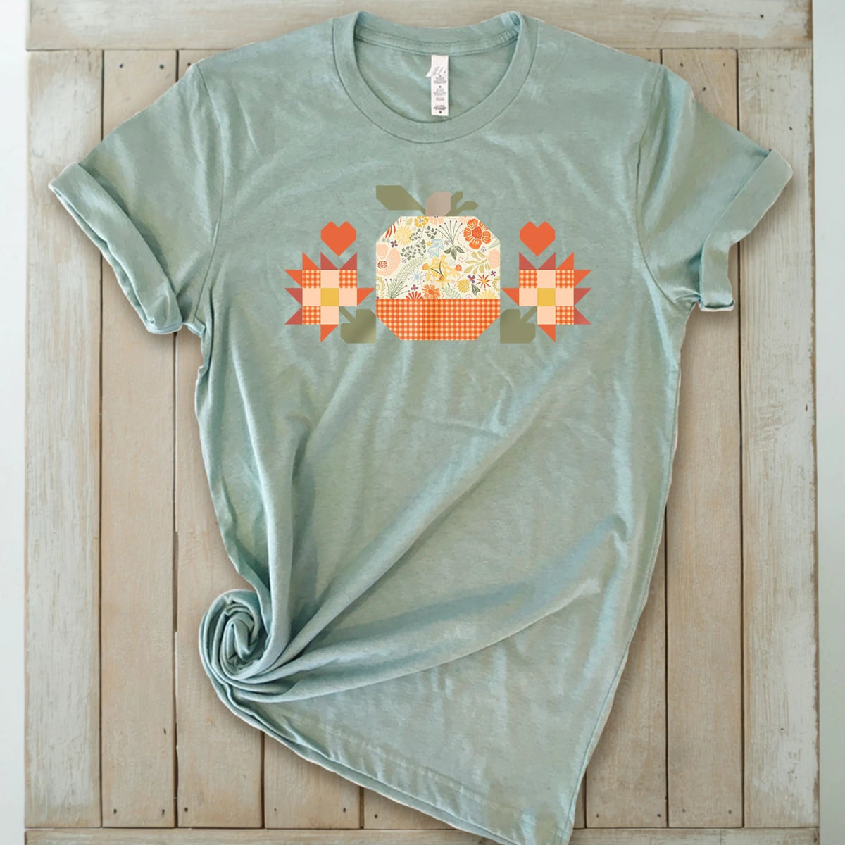 Falling for Fall patchwork pumpkin with quilt-block stars and hearts on a t-shirt in sage, styled on wood – Kate Spain design for Pat Sloan