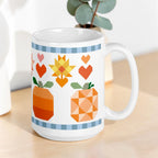 15 oz ceramic mug with the Falling for Fall patchwork pumpkin, quilt-block stars and hearts, styled with a plant – Kate Spain design for Pat Sloan