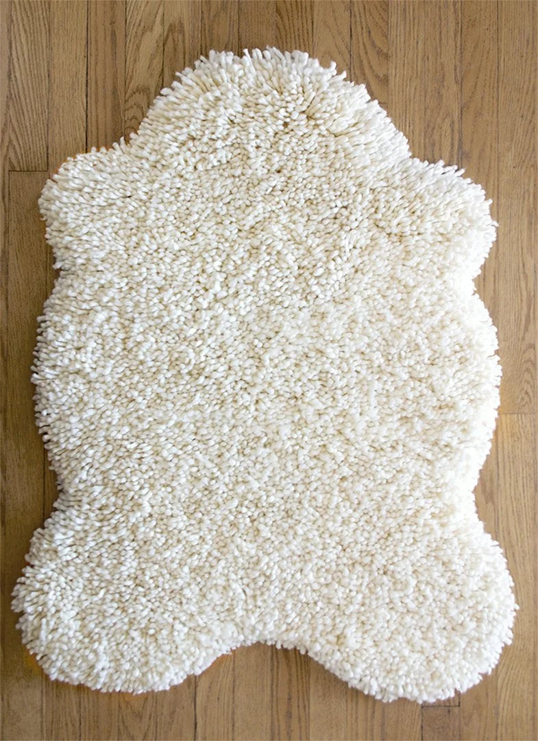nothing to hide hand-knotted shag throw rug in undyed natural white New Zealand wool, 28 by 39 inch hide shape on a wood floor – Kate Spain design