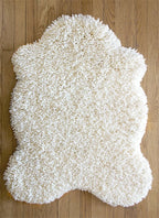 nothing to hide hand-knotted shag throw rug in undyed natural white New Zealand wool, 28 by 39 inch hide shape on a wood floor – Kate Spain design