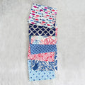 A vertical stack of nine folded fabric squares with various blue, red, and white patterns, displayed on a textured gray concrete surface.
