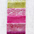 A vertical stack of five folded fabric strips in shades of yellow-green, white with pink floral patterns, solid hot pink, white with dark pink floral patterns, and dark magenta, laid flat on a white textured fabric background.