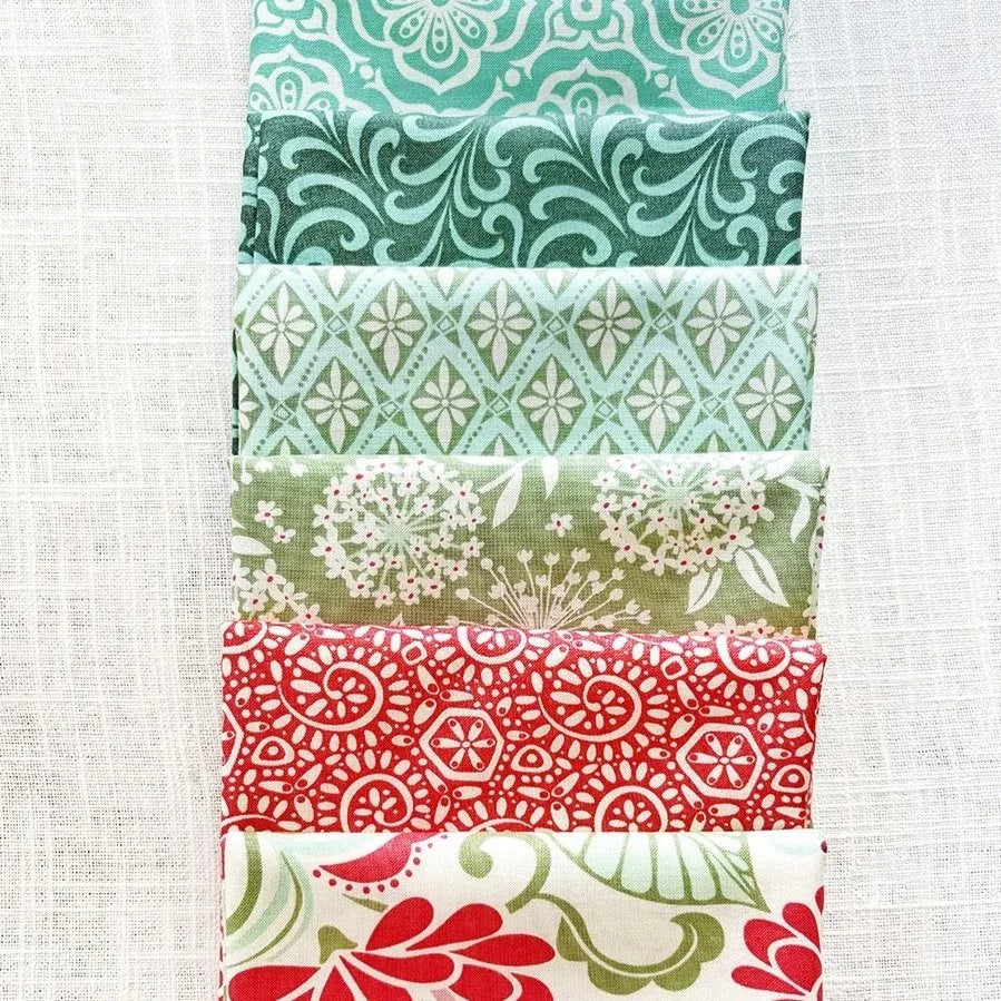 Five folded fabric pieces stacked vertically, each with a different pattern in teal, sage green, red, and cream, displayed on a textured white linen background.