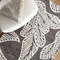 eye heart hand Taupe Leaf hand-tufted wool rug with oversized cream leaves on taupe, close-up beneath a white chair – Kate Spain design