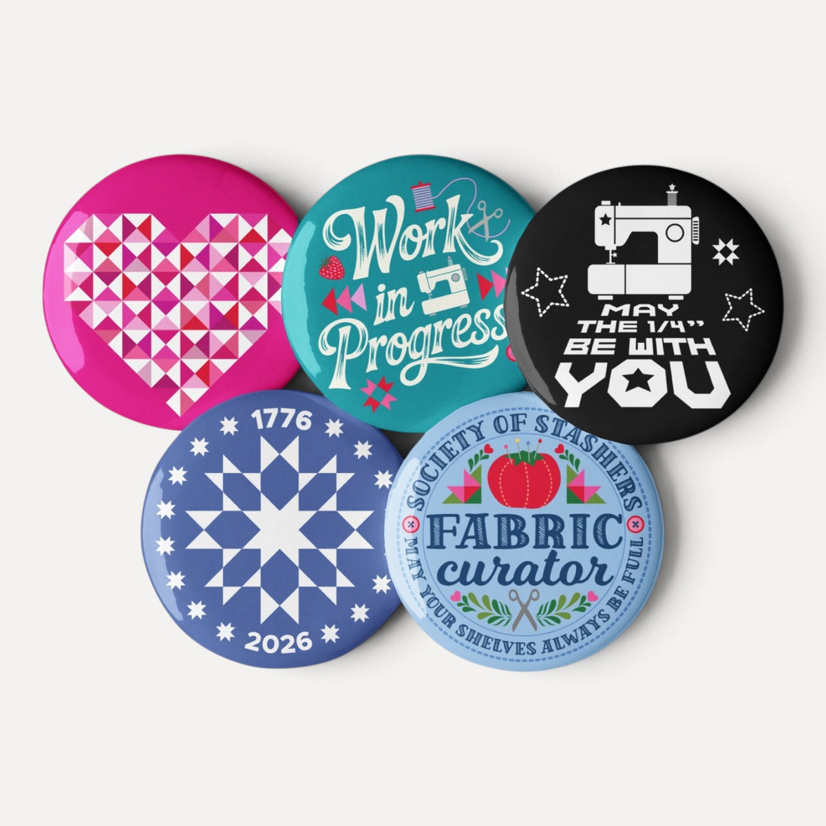 Sloan Zone Celebration pin button set of five with patchwork heart, Work in Progress, May the ¼" Be With You, 1776–2026 quilt star and Fabric Curator designs, buttons grouped together – Kate Spain design for Pat Sloan