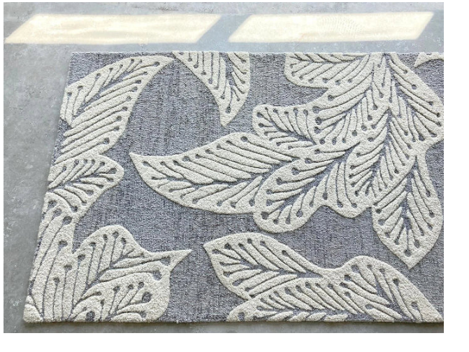 eye heart hand Grey Leaf hand-tufted wool rug with oversized cream leaves on grey, on a concrete floor, angled view – Kate Spain design
