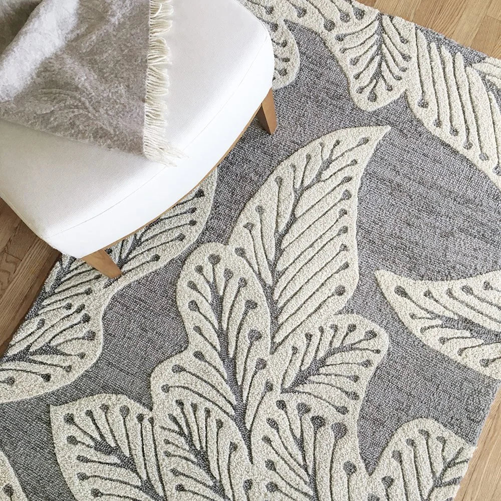 eye heart hand Grey Leaf hand-tufted wool rug with oversized cream leaves on grey, close-up beneath a white chair – Kate Spain design