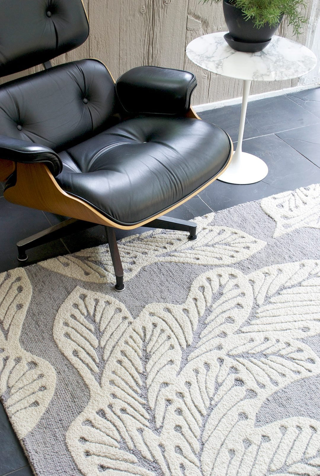 eye heart hand Grey Leaf hand-tufted wool rug with oversized cream leaves on grey, beneath a black leather lounge chair – Kate Spain design