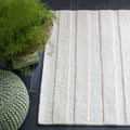 eye heart hand Pure Stripe hand-tufted rug in undyed natural white wool with subtle tonal stripes, on a slate floor beside a knit pouf and fern – Kate Spain design
