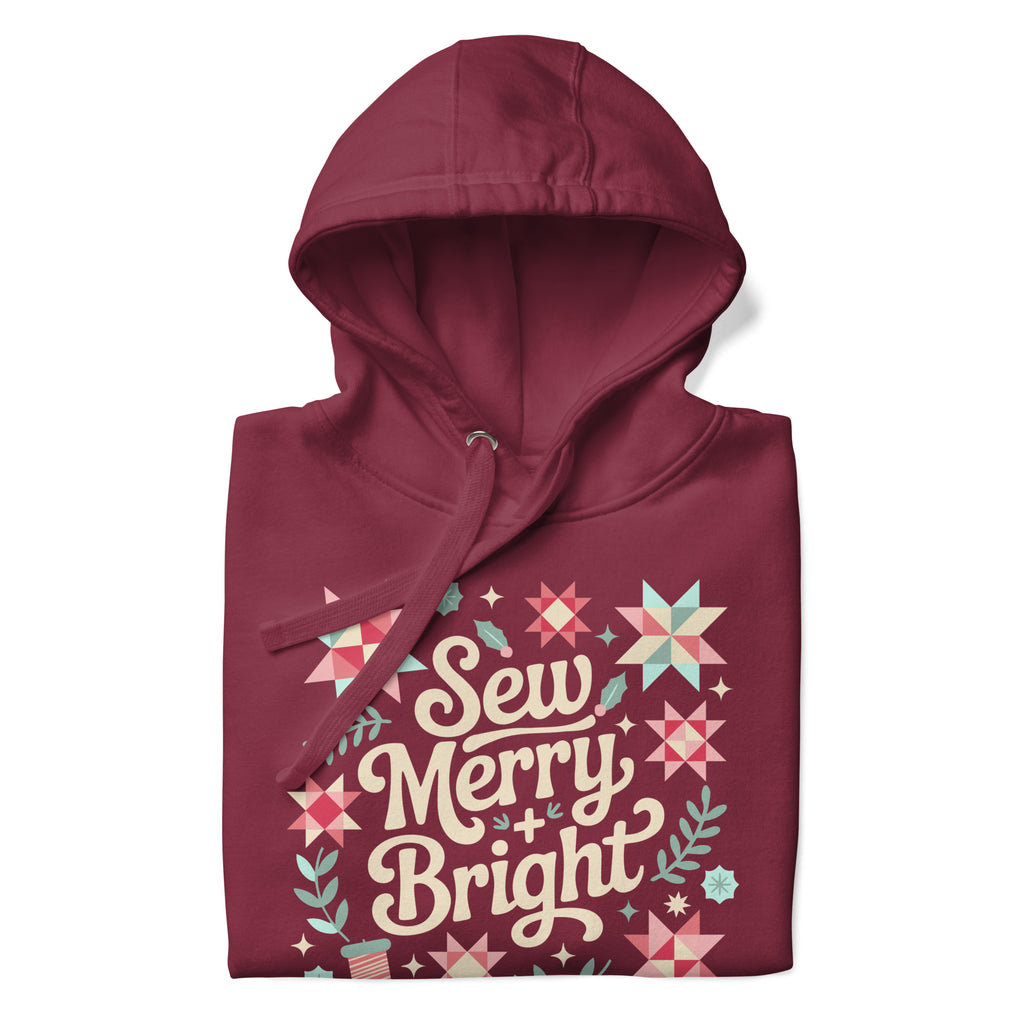 Sew Merry + Bright lettering with quilt-block stars, holly and a thread spool on a pullover hoodie in maroon, folded close-up of the design – Kate Spain design for Pat Sloan
