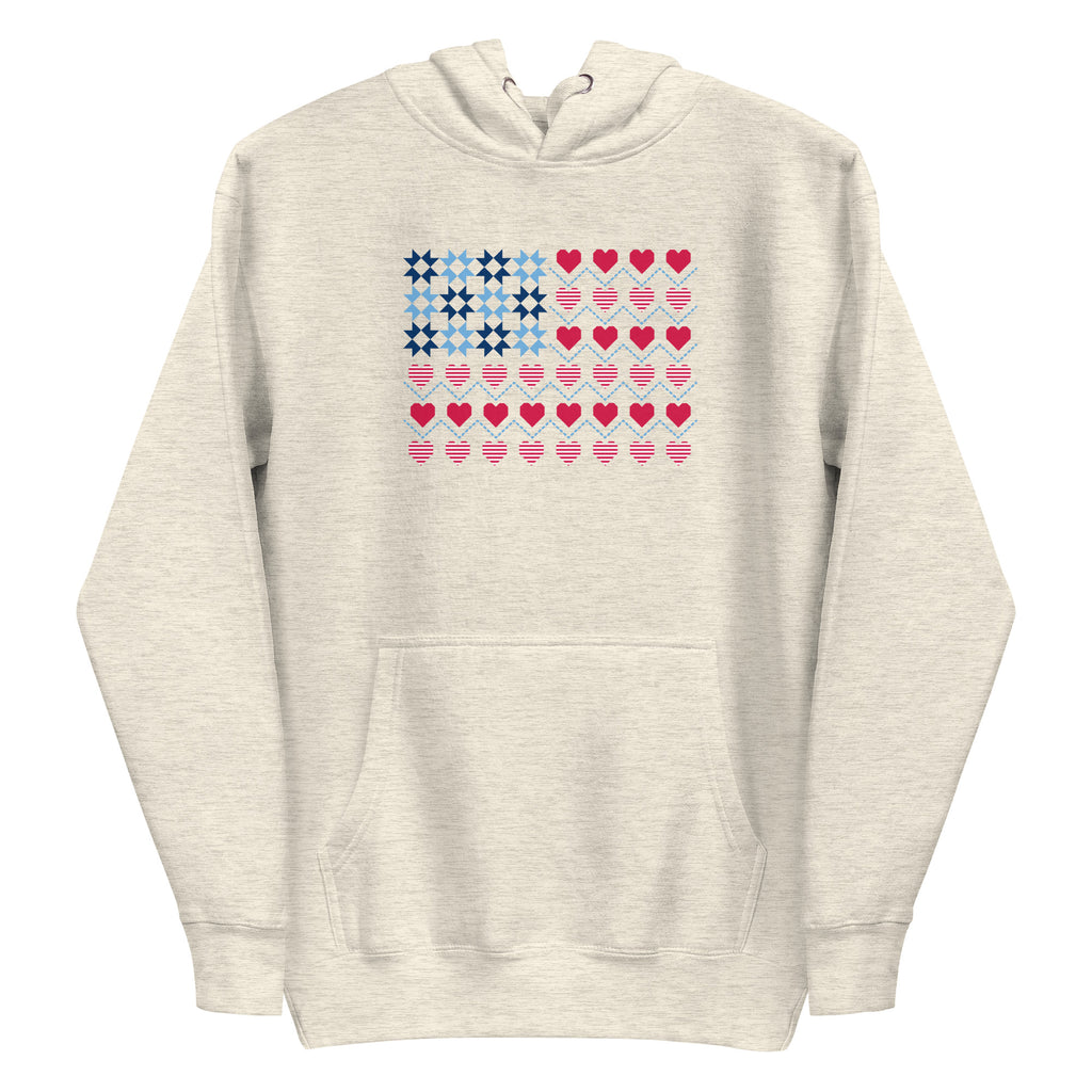 United We Quilt patchwork flag with quilt-block stars and heart stripes on a pullover hoodie in natural heather, front view – Kate Spain design for Pat Sloan