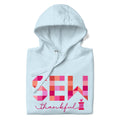 Sew Thankful patchwork lettering with a heart-topped thread spool on a pullover hoodie in sky blue, folded close-up of the design – Kate Spain design for Pat Sloan