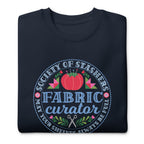 Fabric Curator Society of Stashers badge with a tomato pincushion on a crewneck sweatshirt in navy, folded close-up of the design – Kate Spain design for Pat Sloan