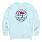 Fabric Curator Society of Stashers badge with a tomato pincushion on a crewneck sweatshirt in sky blue, front view – Kate Spain design for Pat Sloan