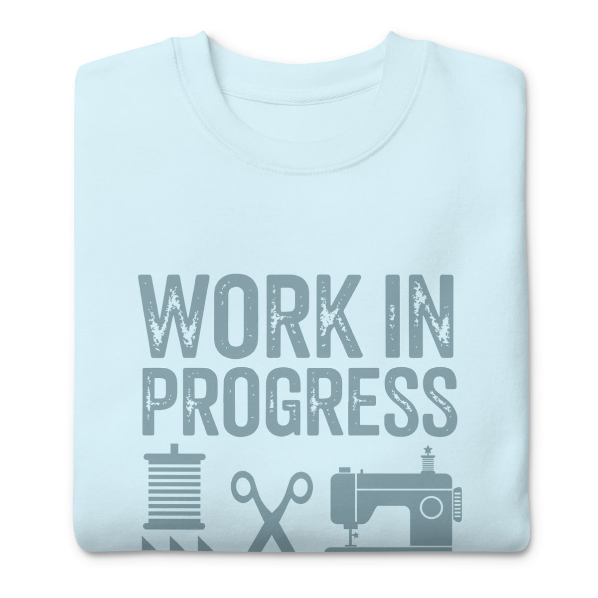 Work in Progress lettering with sewing icons on a premium sweatshirt in sky blue, folded close-up of the design – Kate Spain design for Pat Sloan