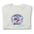 Quilters United quilt badge in red, white and blue on a t-shirt in ash, folded close-up of the design – Kate Spain design for Pat Sloan