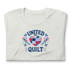 Quilters United quilt badge in red, white and blue on a t-shirt in ash, folded close-up of the design – Kate Spain design for Pat Sloan