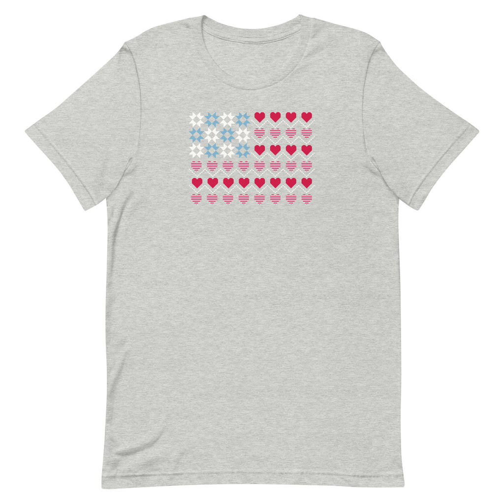 United We Quilt patchwork flag with quilt-block stars and heart stripes on a t-shirt in athletic heather grey, front view – Kate Spain design for Pat Sloan