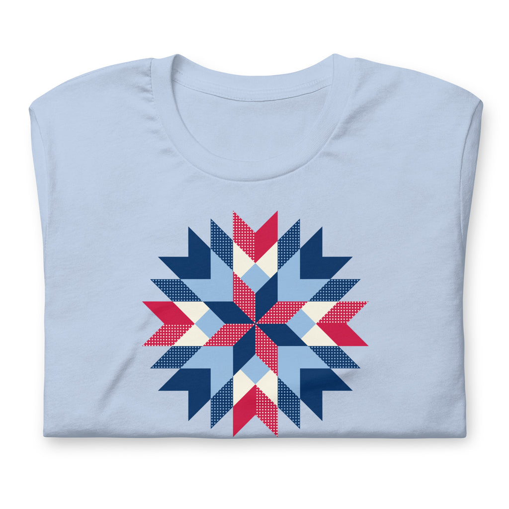 Barn Star quilt block in red, white and blue on a t-shirt in baby blue, folded close-up of the design – Kate Spain design for Pat Sloan
