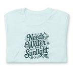 Needs Water + Sunlight hand lettering with leaf and sun accents on a t-shirt in heather ice blue, folded close-up of the design – Kate Spain design