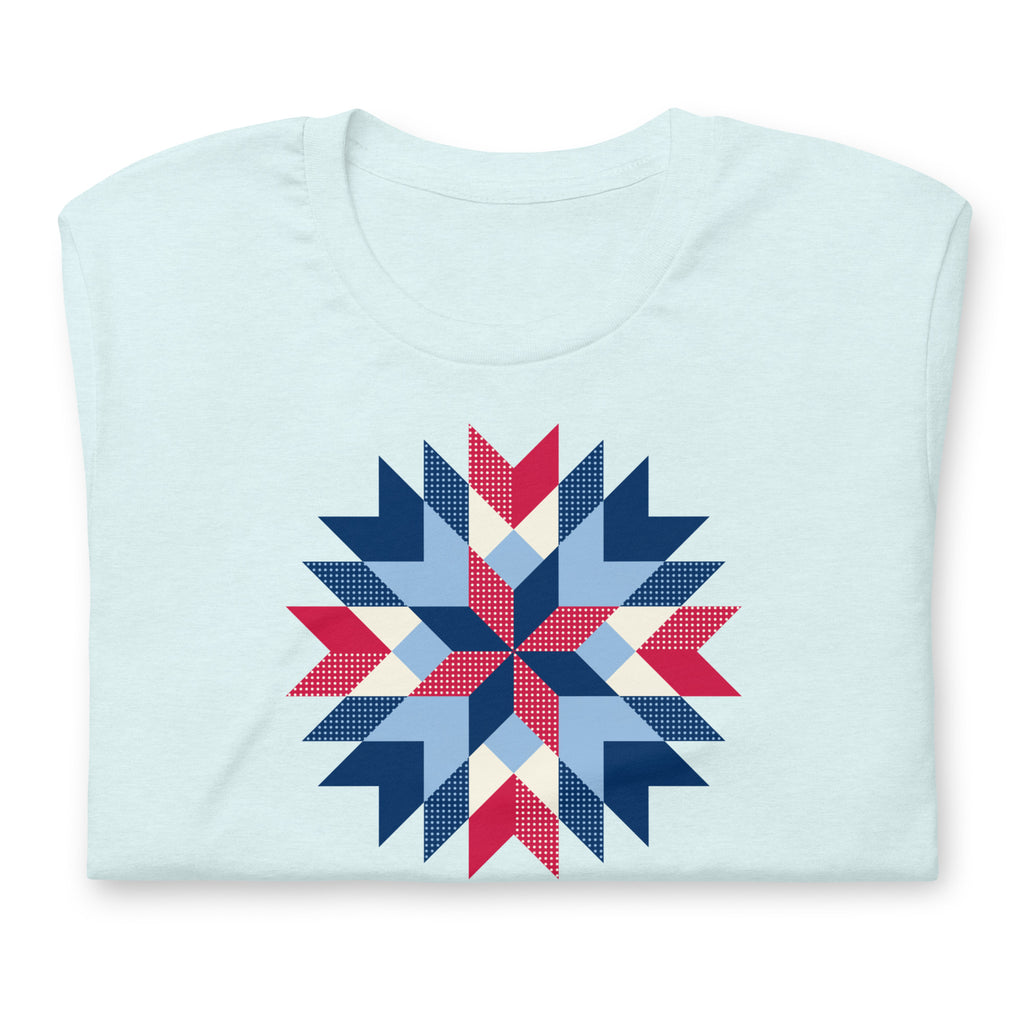 Barn Star quilt block in red, white and blue on a t-shirt in heather ice blue, folded close-up of the design – Kate Spain design for Pat Sloan