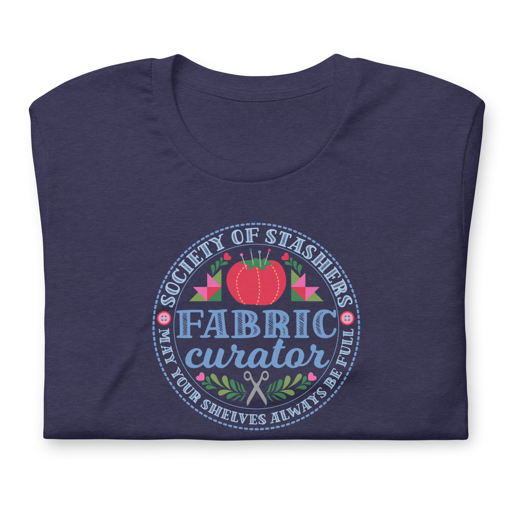Fabric Curator Society of Stashers badge with a tomato pincushion on a t-shirt in heather navy, folded close-up of the design – Kate Spain design for Pat Sloan