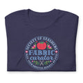 Fabric Curator Society of Stashers badge with a tomato pincushion on a t-shirt in heather navy, folded close-up of the design – Kate Spain design for Pat Sloan