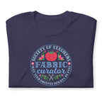 Fabric Curator Society of Stashers badge with a tomato pincushion on a t-shirt in heather navy, folded close-up of the design – Kate Spain design for Pat Sloan
