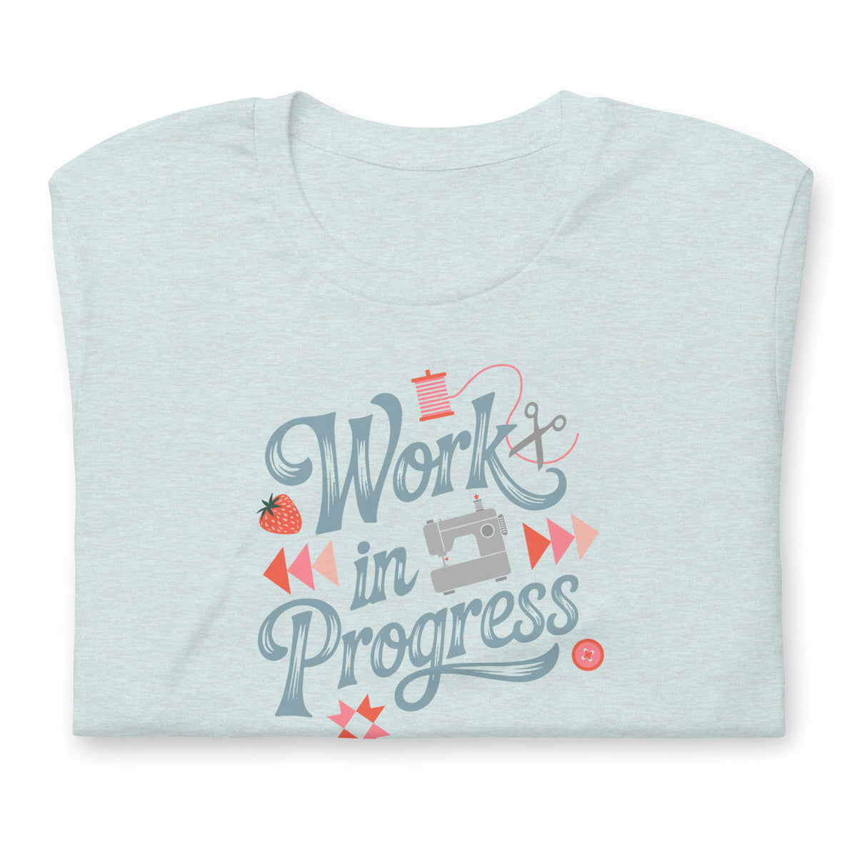 Work in Progress sewing design with flying geese, sewing machine, strawberry and thread spool on a t-shirt in heather prism ice blue, folded close-up of the design – Kate Spain design for Pat Sloan