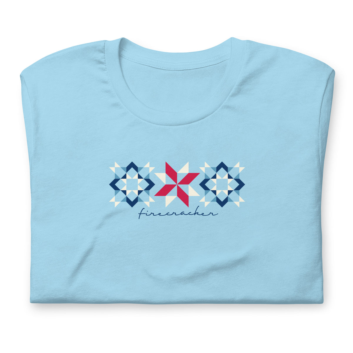 Firecracker quilt-block stars with script lettering in red, white and blue on a t-shirt in ocean blue, folded close-up of the design – Kate Spain design for Pat Sloan