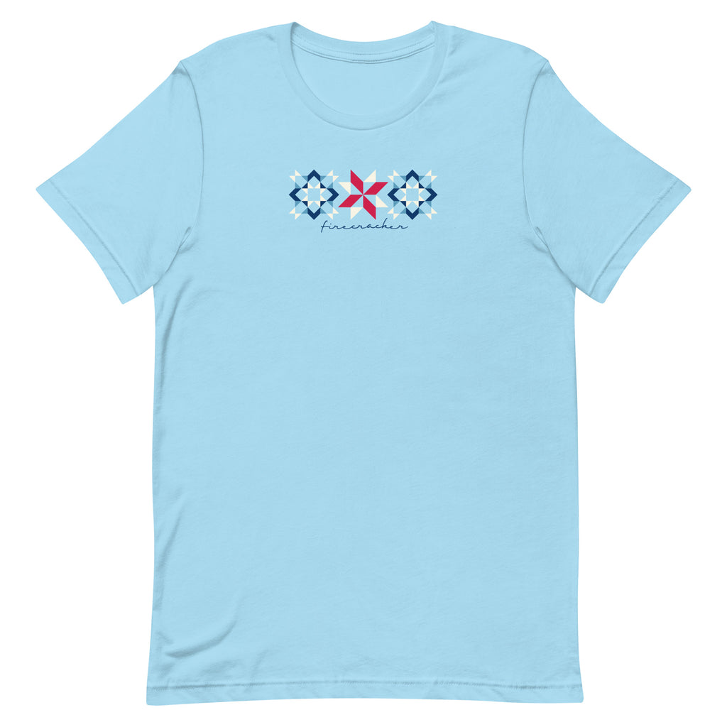 Firecracker quilt-block stars with script lettering in red, white and blue on a t-shirt in ocean blue, front view – Kate Spain design for Pat Sloan