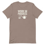 Garden Work in Progress distressed lettering with a shovel, pitchfork and watering can on a t-shirt in pebble, front view – Kate Spain design