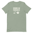 Garden Work in Progress distressed lettering with a shovel, pitchfork and watering can on a t-shirt in sage, front view – Kate Spain design