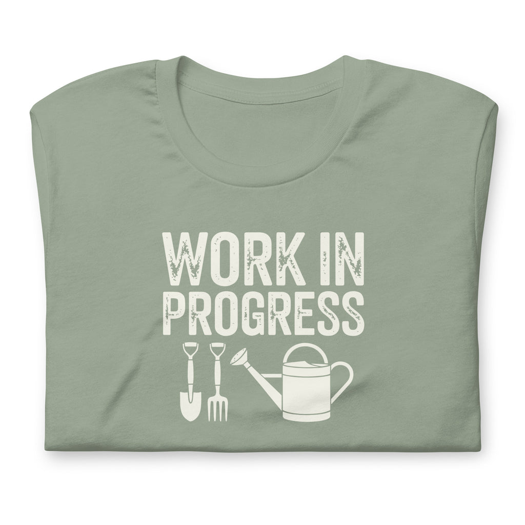 Garden Work in Progress distressed lettering with a shovel, pitchfork and watering can on a t-shirt in sage, folded close-up of the design – Kate Spain design