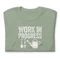 Garden Work in Progress distressed lettering with a shovel, pitchfork and watering can on a t-shirt in sage, folded close-up of the design – Kate Spain design
