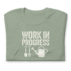 Garden Work in Progress distressed lettering with a shovel, pitchfork and watering can on a t-shirt in sage, folded close-up of the design – Kate Spain design