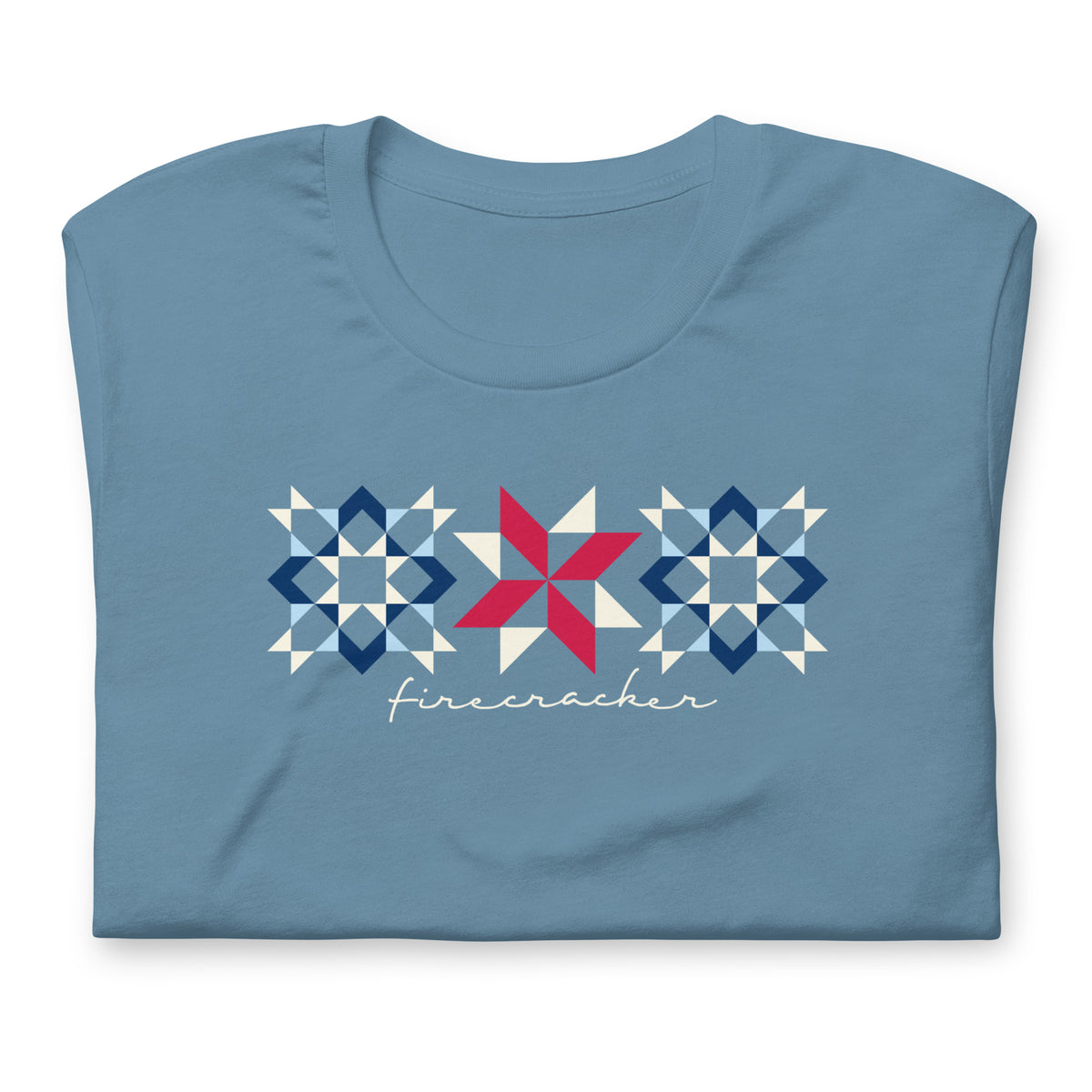 Firecracker quilt-block stars with script lettering in red, white and blue on a t-shirt in steel blue, folded close-up of the design – Kate Spain design for Pat Sloan