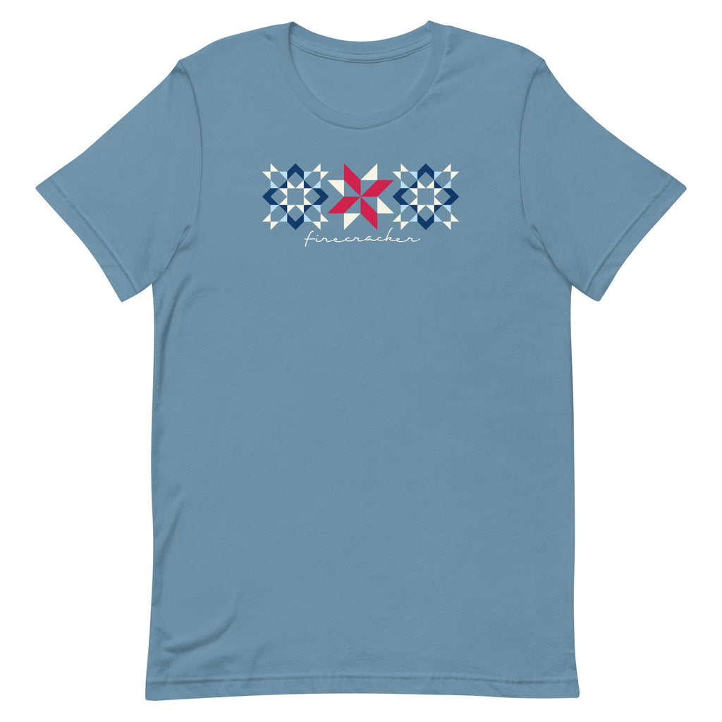 Firecracker quilt-block stars with script lettering in red, white and blue on a t-shirt in steel blue, front view – Kate Spain design for Pat Sloan