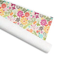 Terrain gift wrap, hot pink, orange, yellow, mauve and aqua flowers with ferns and vines on white, 30 by 36 inch matte paper, shown partly rolled – Kate Spain design