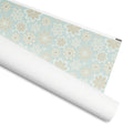 Flurry gift wrap, white and gold snowflakes on powder blue dots, 30 by 36 inch matte paper, shown partly rolled – Kate Spain design